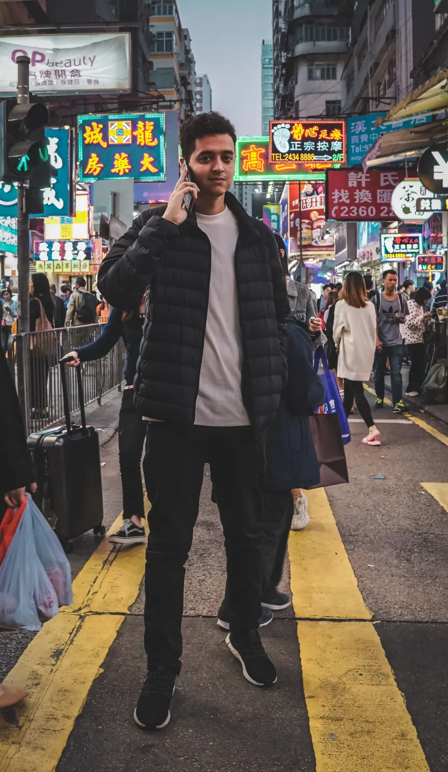 Gabriel ao telefone com uma mala, numa rua de neon em Hong Kong